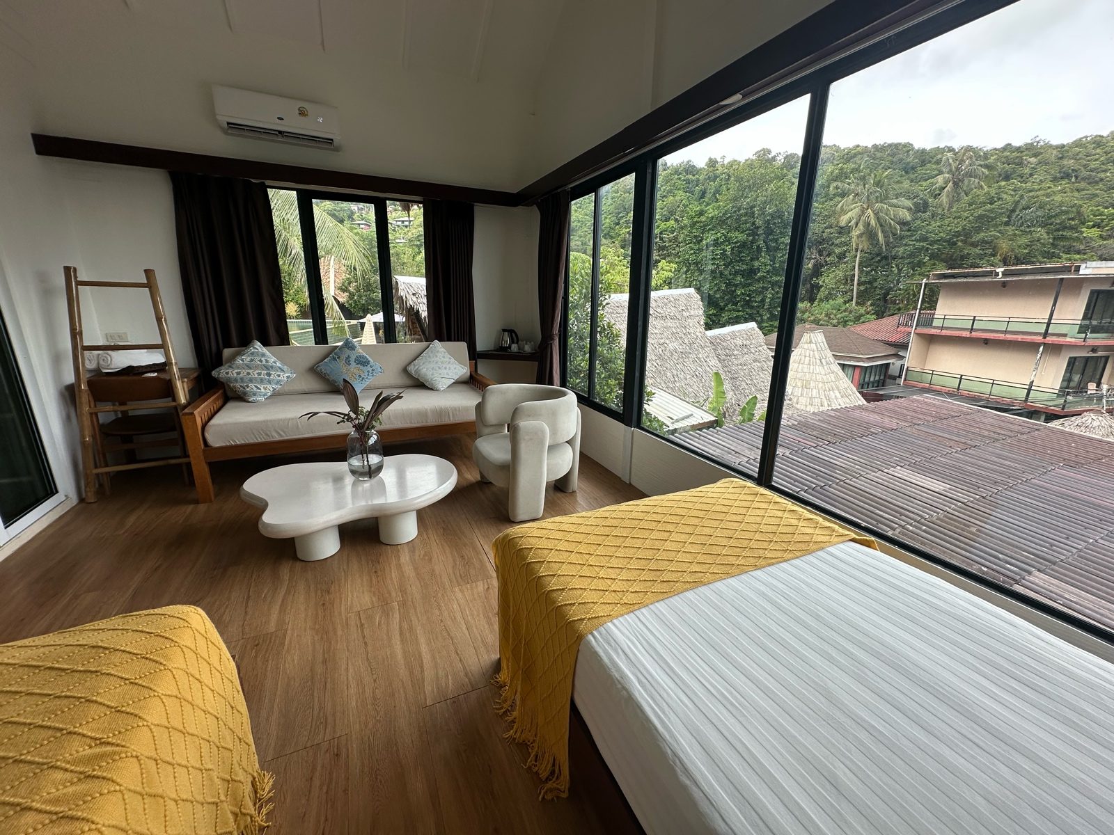 Sitting area of a Phi Phi cottage with a sofa, two beds and a kettle station, straight off the phone: the floor reads grey and the windows are winning.