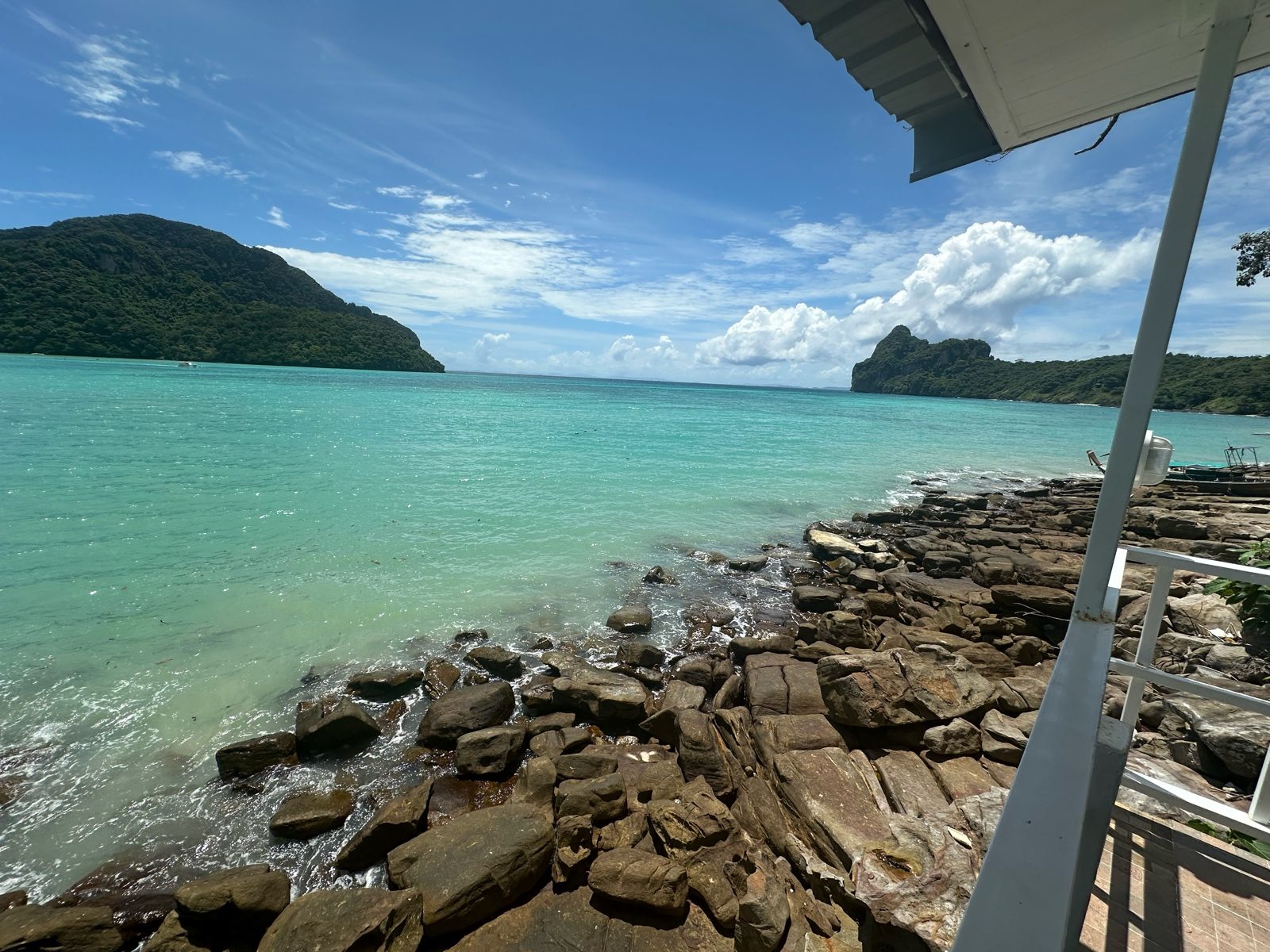 Before: a rocky shoreline seen from a balcony, the sea a flat teal and the sky low in contrast.
